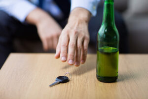 alcohol abuse, drunk driving, risking a DUI charge - close up of beer bottle and male driver hand taking car key from table