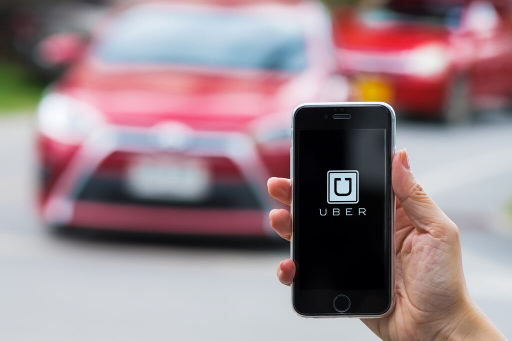 CHIANG MAITHAILAND - JUL 242016 : A MAN hand holding Uber app showing on iphone 6s on road and red car. Uber is smartphone app-based transportation network