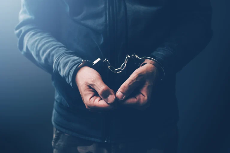 Arrested computer hacker and cyber criminal with handcuffs close up of hands