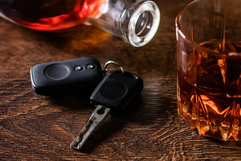 Alcoholic drink in a glass and car keys on a wooden desk. Drunk driving concept