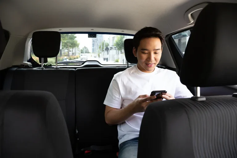 Asian young man using a smartphone in back seat of car, Passengers use an app to order a ride and Peer-to-peer ridesharing concept