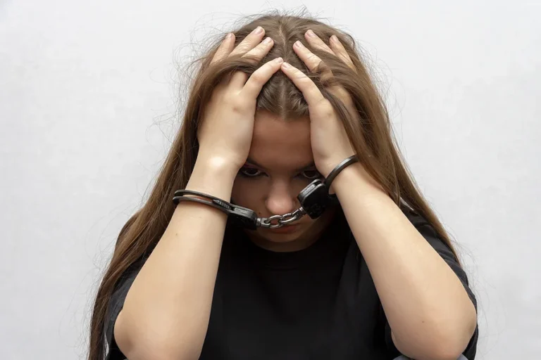 A young girl handcuffed hides her face on a gray background, close-up. Juvenile delinquent in a black T-shirt, criminal liability of minors 50.