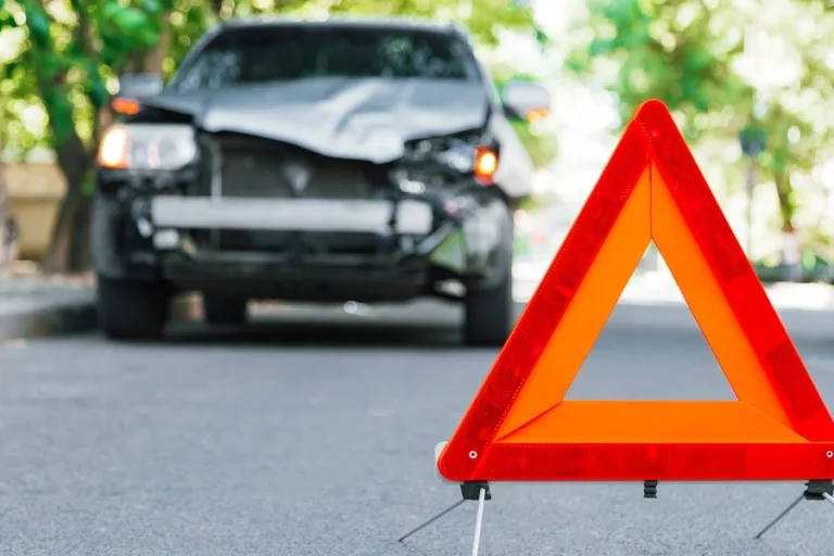 Red emergency stop triangle sign on road during a car accident. Broken gray car during road traffic accident. Car crash traffic accident on city road after collision. Long web banner