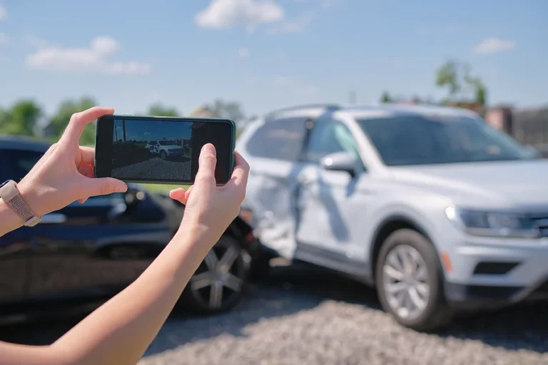 Female driver hands photographing on sellphone camera wrecked vehicles on street side for insurance service after car accident. Road safety concept.