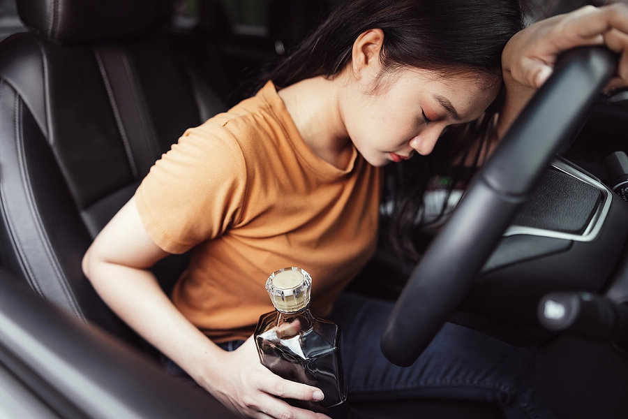 young asian woman with a bottle of alcohol behind the wheel of a car facing a dui charge